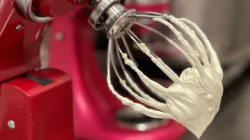 Mixer whisk with cream, red kitchen appliance.