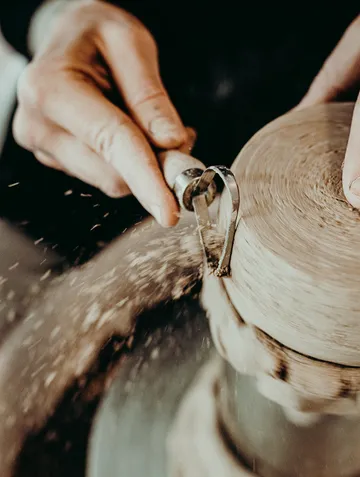 Hands carving wood on a lathe, creating sawdust.