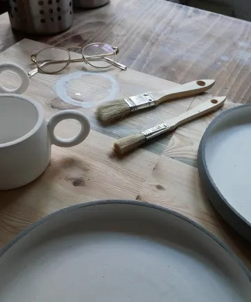 Paintbrushes, ceramics, glasses on wooden table.