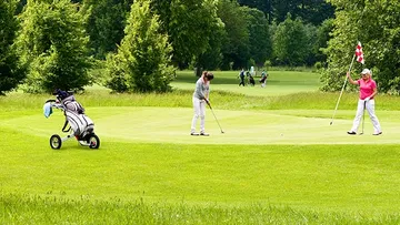 Zwei Golfer auf dem Grün, einer puttet.