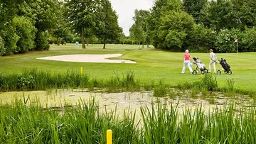 Two golfers walk on lush golf course.