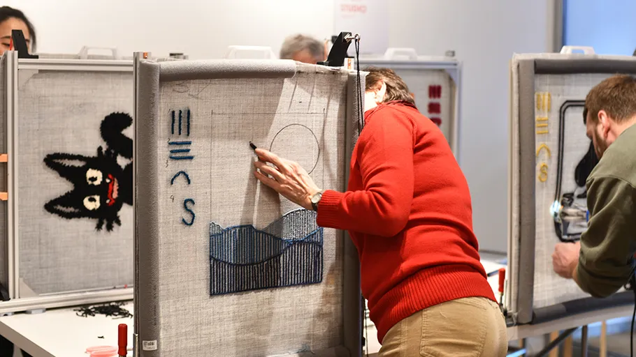 People embroidering designs in workshop setting.