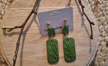 Green leaf earrings on a wooden surface.