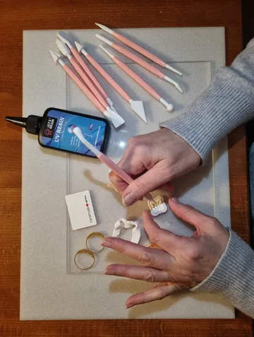 Person crafting jewelry with UV resin tools.