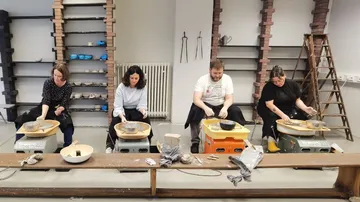 Four people crafting pottery on electric wheels.