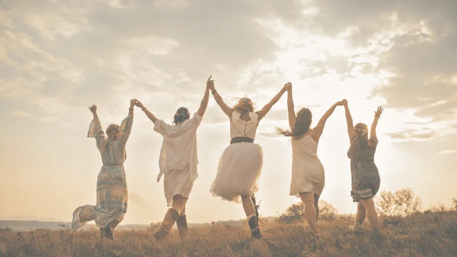 Group of women dancing outdoors, holding hands.