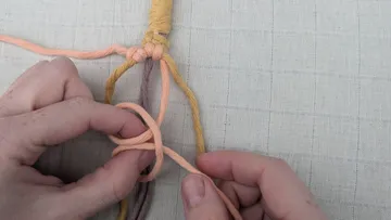 Hands knotting colorful yarn strands on fabric.