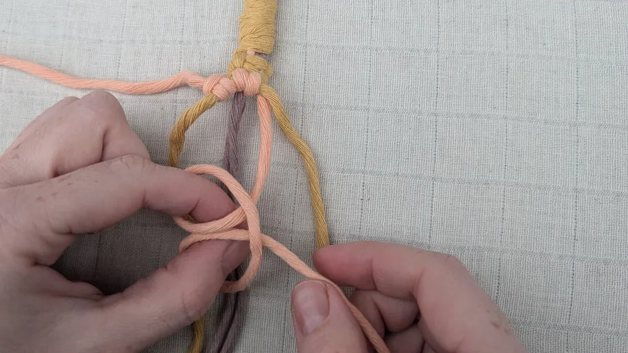 Hands knotting colorful yarn strands on fabric.