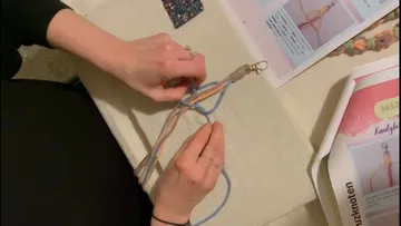 Hände flechten bunte Fäden auf Tisch.