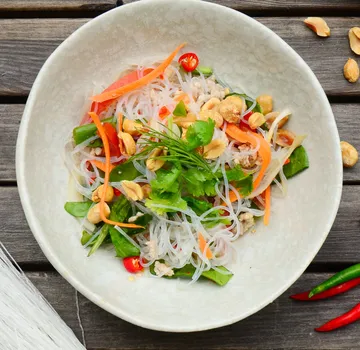 Noodle salad with vegetables on wooden table.