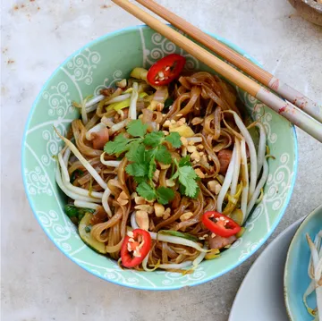 Noodles with vegetables and chopsticks on bowl.