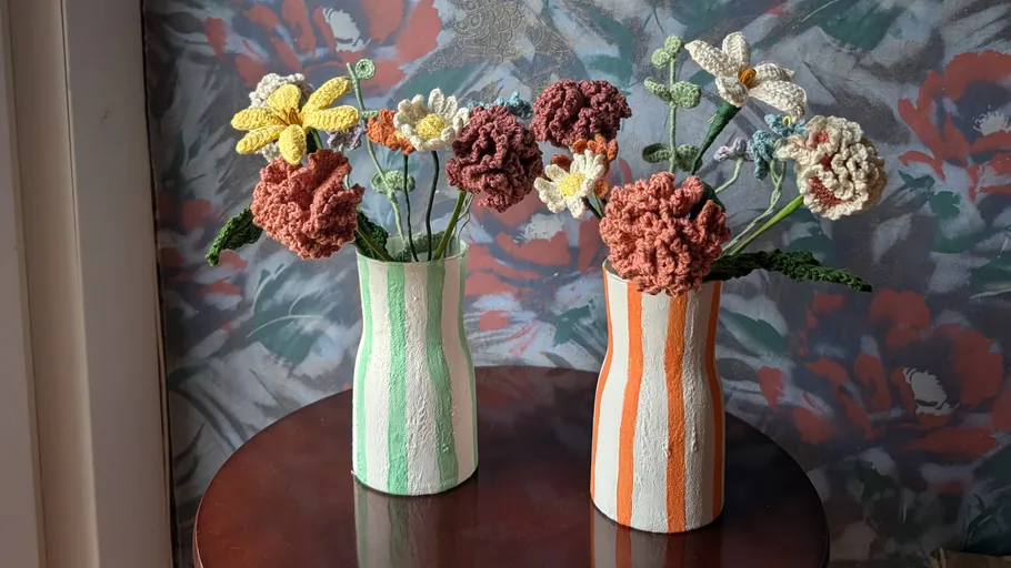 Crochet flowers in striped vases on table.