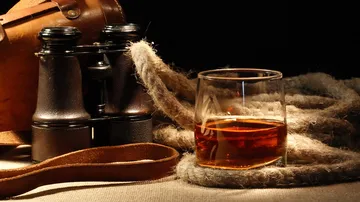 Binoculars, whiskey glass, rope on table.