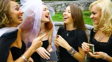 Four women laughing outdoors, one wearing a veil.