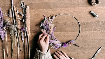 Hände fertigen Blumenkranz auf Holztisch.