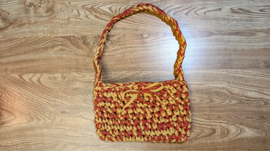 Woven handbag with red-yellow pattern on wood surface.
