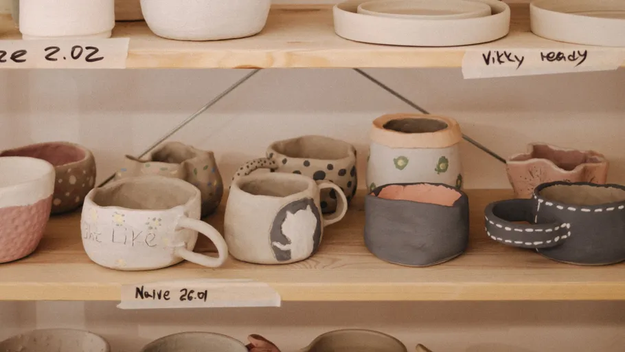 Handgefertigte Keramiktassen auf Holzregalen.