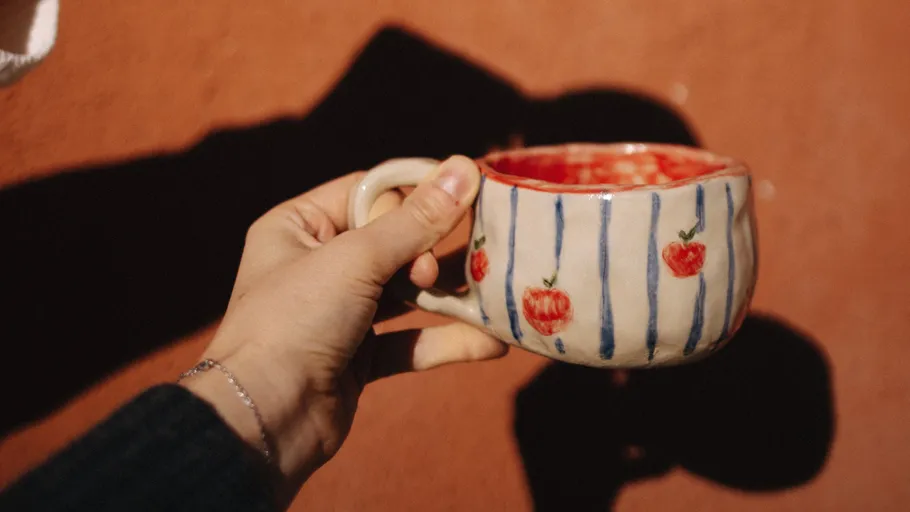 Hand hält Tasse mit Apfeldesign draußen.