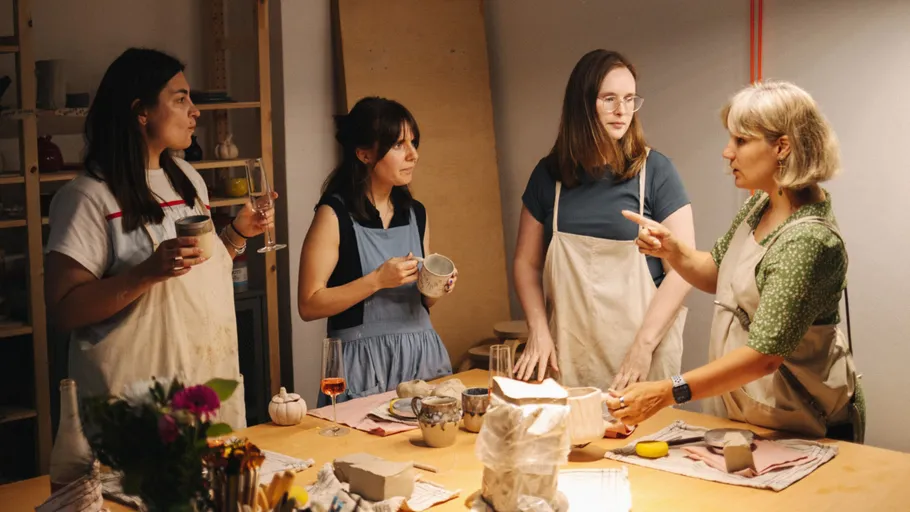 Four women in aprons discussing pottery workshop.