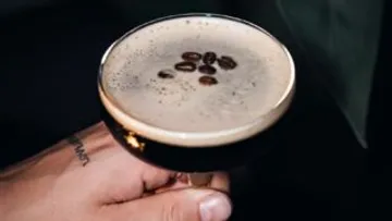 Hand hält Espresso-Martini bei schwacher Beleuchtung.