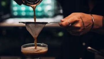 Hand gießt Kaffee durch ein Sieb.