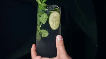 Hand hält Cocktail mit Minze und Gurke.