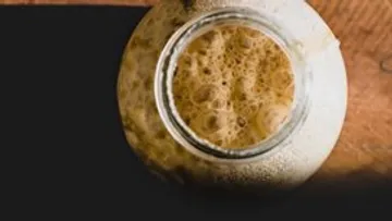 Bubbly liquid in a glass jar, wooden surface.