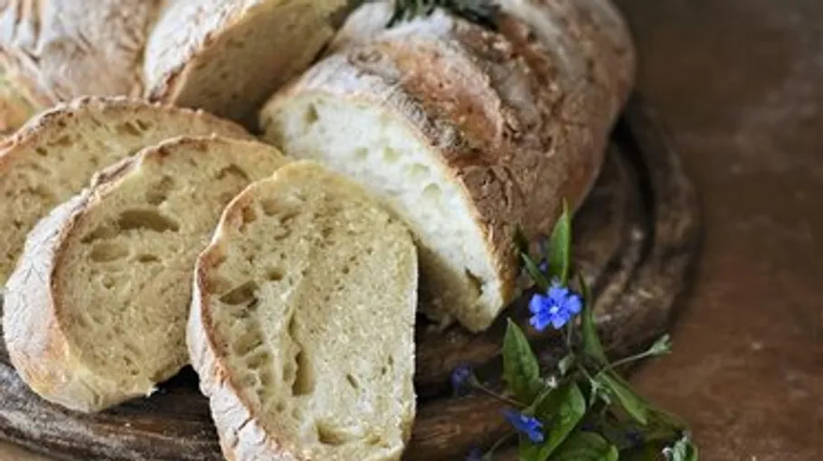Sliced bread loaf on wooden board, flowers nearby.