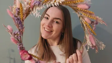 Frau lächelt, hält Blumenkranz im Innenbereich.