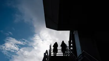 Zwei Personen auf Treppe, bewölkter Himmel.