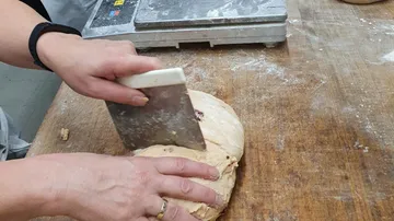Hände schneiden Teig auf Holzarbeitsplatte.