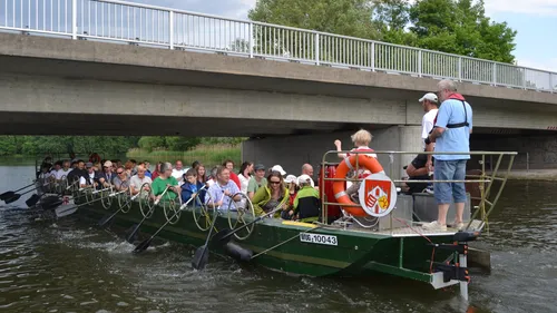 Crowded boat paddling under concrete bridge.