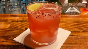 Rosa Cocktail mit Limette auf Holztresen.