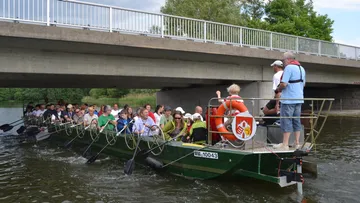 Menschen rudern großes Boot unter Brücke.
