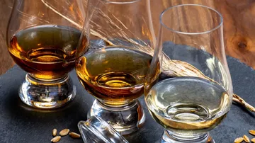 Drei Gläser Whiskey auf Holztisch.