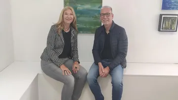 Two people smiling, sitting in an art gallery.