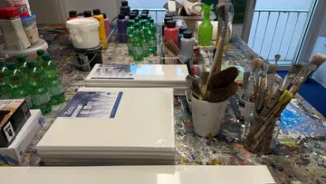 Kunstbedarf auf einem farbbespritzten Tisch.