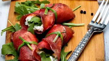 Meat wraps filled with cheese on cutting board.