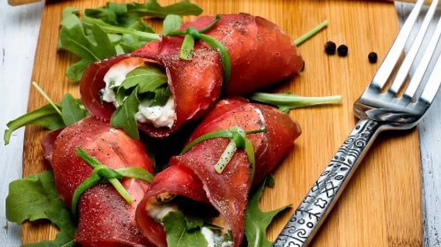 Meat wraps filled with cheese on cutting board.