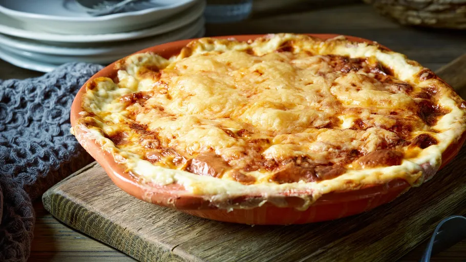 Cheesy pizza in round dish on wooden table.