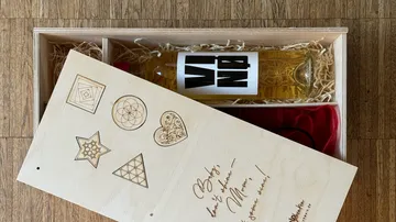 Holzkiste mit dekoriertem Deckel und Flasche darin.