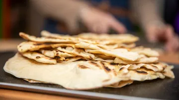 Flatbreads stacked on table, person in background.