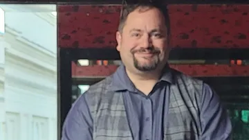Man smiling indoors with red wall background.