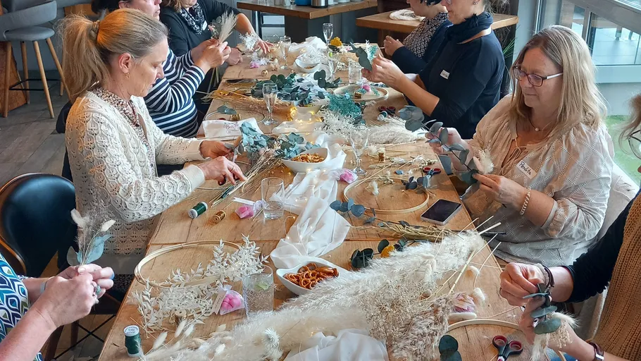 Women crafting wreaths around a wooden table.