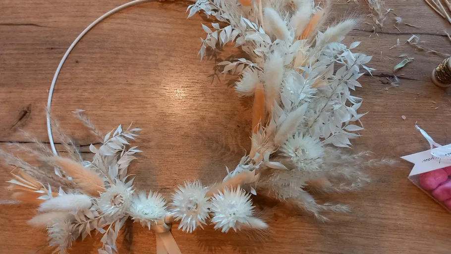 Floral wreath with dried white flowers on table.