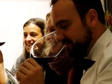 Ein Mann riecht Wein, umgeben von lachenden Freunden.