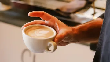 Hand holding latte cup with art, cafe background.