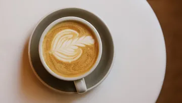 Kaffeetasse mit Latte Art auf Tisch.