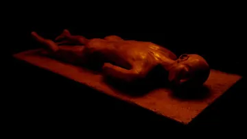 Sculpture of man lying on slab, dark lighting.