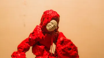 Red sculpture with white face, beige background.